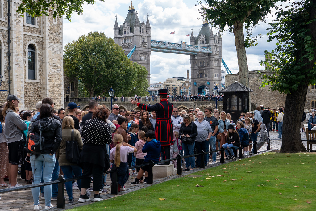 A Yeoman Warder, or Beefeater, leading a tour at the Tower of London with Tower Bridge behind
